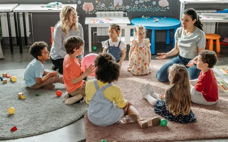 Halıda çember olmuş çocuklar ve öğretmenleri